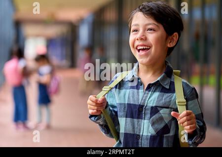 Portrait Of Smiling Male Elementary School Pupil Outdoors With Backpack At School Stock Photo