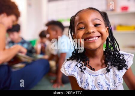 Portrait Of Smiling Female Elementary School Pupil Sitting In Classroom At School Stock Photo