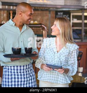 Female Manager Holding Digital Tablet Working With Staff In Restaurant Or Coffee Shop Stock Photo
