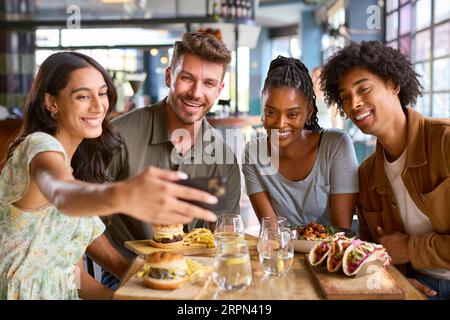 Group Of Friends Meeting Up In Restaurant Posing For Selfie On Mobile Phone With Food Stock Photo