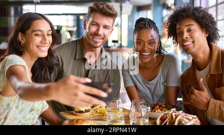 Group Of Friends Meeting Up In Restaurant Posing For Selfie On Mobile Phone With Food Stock Photo