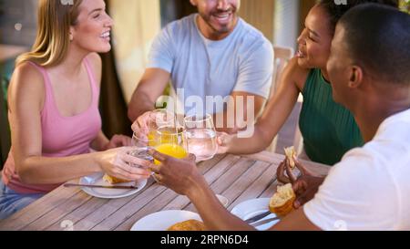 Group Of Smiling Multi-Cultural Friends Eating Breakfast Outdoors At Home Making A Toast Together Stock Photo