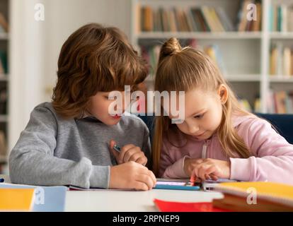 School kids friends using smartphone and playing games online, sitting in classroom interior Stock Photo