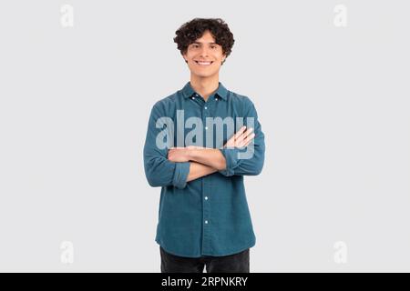 Positive Curly Young Man Posing Crossing Hands Over White Background Stock Photo