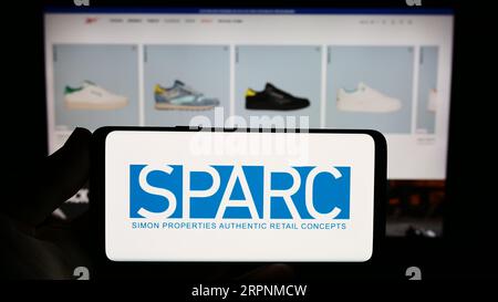 Person holding smartphone with logo of US retail company SPARC Group LLC on screen in front of website. Focus on phone display. Stock Photo