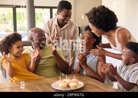 Multi-Generation Family Celebrate Grandmother's Birthday With Cake And Candles Around Table At Home Stock Photo