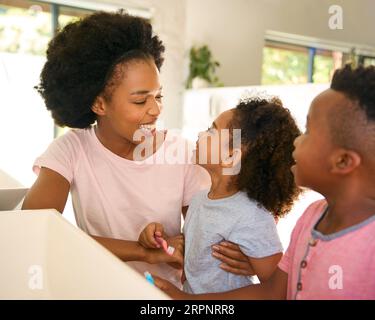 Mother Helping Children Brushing Teeth In Bathroom At Home Before Bed Stock Photo