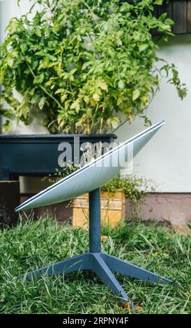 GErmany - Aug 12, 2023: Side view of Starlink dish antenna for reliable internet satellite transmission in remote area - green tomatoes plants in background Stock Photo