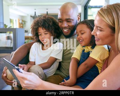 Smiling Family Sitting On Sofa Using Digital Tablet At Home Together Stock Photo