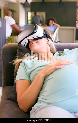 Pregnant Woman At Home Lying On Sofa Wearing VR Headset Stock Photo