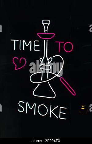 Neon sign on a black background, white pink text Time to smoke and image of a hookah Stock Photo