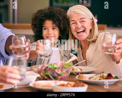 Multi-Generation Family Doing Cheers With Water As They Sit Around Table Having Meal At Home Stock Photo