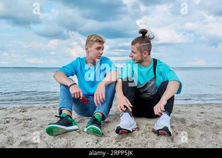 Young teenage male friends sitting at beach, talking, laughing Stock Photo