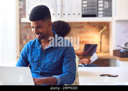 Young Smiling Businessman Working On Laptop At Desk In Office Stock Photo