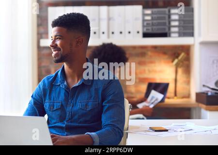 Young Smiling Businessman Working On Laptop At Desk In Office Stock Photo