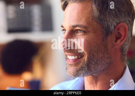 Close Up Portrait Of Smiling Mature Businessman At Desk In Modern Office Stock Photo