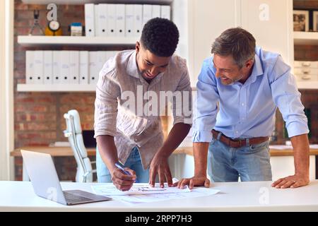 Trainee Male Architect Meeting With Colleague To Discuss Building Plans In Modern Office Stock Photo