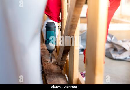 Technician drilling wooden box with drilling machine. Assembly of heavy machinery containers for transport. Technician carpenters wear safety gloves Stock Photo