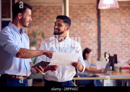 Two Male Business Colleagues With Digital Tablet And Documents Meeting In Busy Office Stock Photo