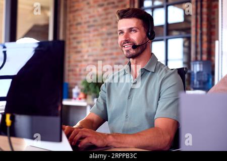 Businessman Wearing Headset At Computer In Customer Support Centre Stock Photo