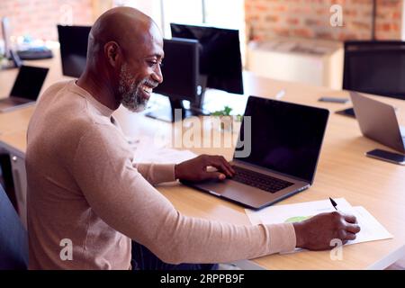 Mature Businessman Working On Laptop At Desk In Modern Office Stock Photo