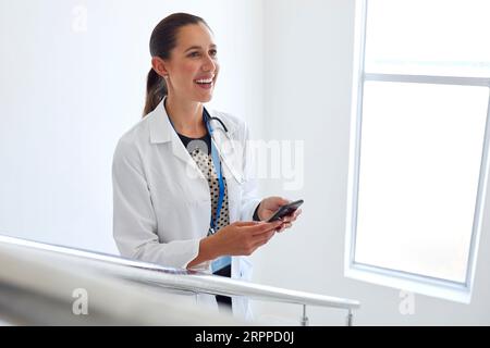 Female Doctor In White Coat Browsing On Mobile Phone On Stairs In Hospital Stock Photo