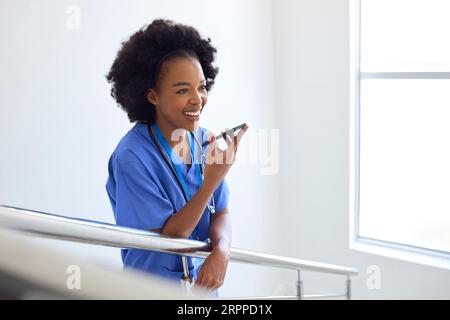 Female Doctor Or Nurse Talking Into Mic Of Mobile Phone On Stairs In Hospital Stock Photo