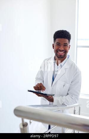 Portrait Of Male Doctor With Digital Tablet Checking Patient Notes On Stairs In Hospital Stock Photo