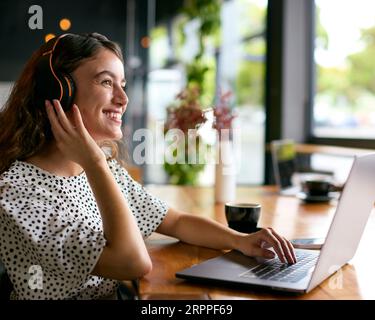 Businesswoman Wearing Wireless Headphones Working On Laptop In Cafe Or Office Stock Photo
