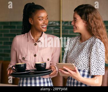 Two Smiling Female Owners Or Staff With Digital Tablet And Cups In Cafe Or Coffee Shop Stock Photo