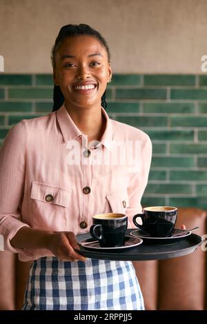 Portrait Of Smiling Female Owner Or Staff Member Carrying Cups In Cafe Or Coffee Shop Stock Photo
