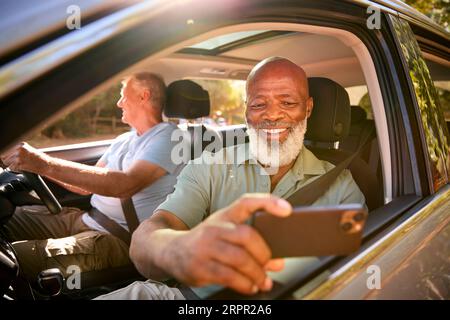 Passenger Taking Selfie On Mobile Phone As Two Senior Male Friends Enjoy Day Trip Out In Car Stock Photo