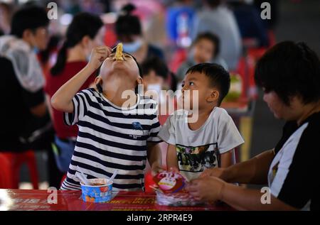 200326 -- HAIKOU, March 26, 2020 -- Children eat snacks at a night market in Haikou, capital of south China s Hainan Province, March 26, 2020. South China s island province of Hainan on Tuesday reduced its existing number of cases of novel coronavirus disease COVID-19 to zero. People s life here is gradually returning to normal.  CHINA-HAINAN-HAIKOU-LIFE-BACK TO NORMAL CN GuoxCheng PUBLICATIONxNOTxINxCHN Stock Photo