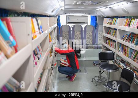 200326 -- CHANGSHA, March 26, 2020 -- A woman selects books in a mobile library in a community of Changsha, central China s Hunan province, March 26, 2020. Recently, the mobile libraries in Changsha have resumed operation amid epidemic prevention and control measures. Mobile library is a project of Changsha Library which takes buses as carriers to visit communities, schools, companies, construction sites and other areas in the city monthly and provide book reading, consulting, borrowing and returning services.  CHINA-HUNAN-CHANGSHA-MOBILE LIBRARY CN ChenxZeguo PUBLICATIONxNOTxINxCHN Stock Photo