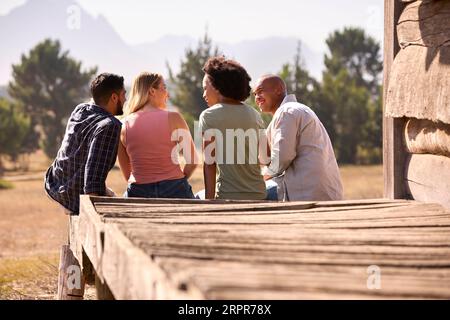 Rear View Of Group Of Friends On Vacation Sitting On Porch Of Countryside Cabin Stock Photo