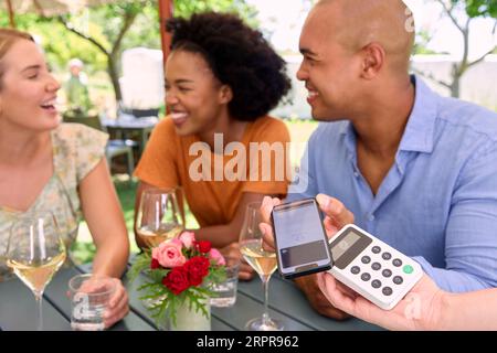 Man Paying Bill At Outdoor Bar Or Restaurant Using Contactless App On Mobile Phone Stock Photo