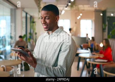 Businessman Standing In Busy Office Using Digital Tablet Stock Photo
