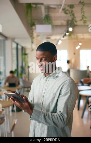 Businessman Standing In Busy Office Using Digital Tablet Stock Photo