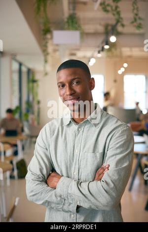 Portrait Of Smiling Businessman Standing In Busy Office Stock Photo