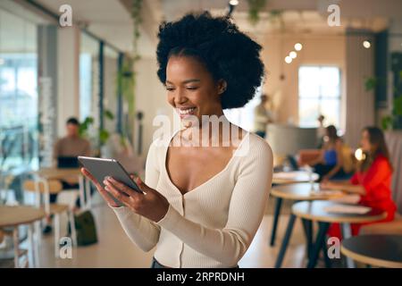 Businesswoman Standing In Busy Office Using Digital Tablet Stock Photo