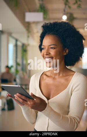 Businesswoman Standing In Busy Office Using Digital Tablet Stock Photo