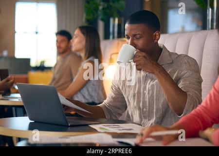 Businessman Drinking Coffee Working On Laptop In Informal Seating Area Of Modern Office Stock Photo