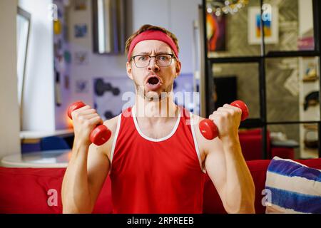 Funny man exercising and doing sport training with small dumbbells in living room. Stock Photo