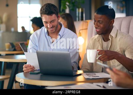 Two Businessmen Working On Laptop In Informal Seating Area Of Modern Office On Coffee Break Stock Photo