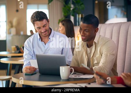 Two Businessmen Working On Laptop In Informal Seating Area Of Modern Office On Coffee Break Stock Photo