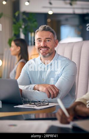 Portrait Of Mature Businessman Working On Laptop In Informal Seating Area Of Modern Office Stock Photo