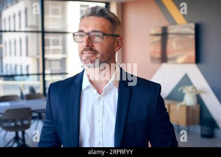 Portrait Of Smiling Mature Businessman Wearing Glasses Standing In Empty Office Stock Photo