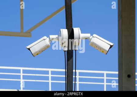 Metal pole with two outdoor security CCTV surveillance cameras in an unfinished building construction site, blue sky background Stock Photo