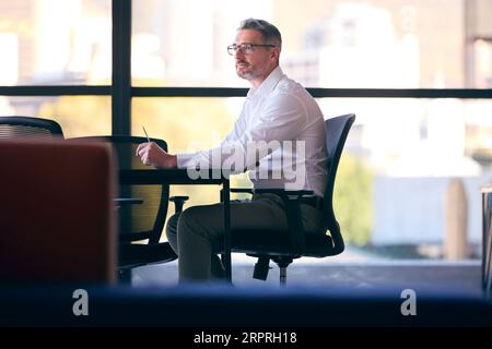 Mature Businessman Working On Laptop Sitting At Boardroom Table Stock Photo
