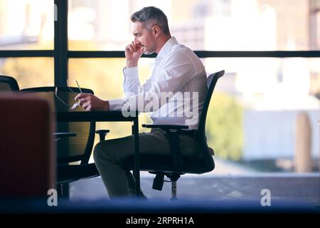 Mature Businessman Working On Laptop Sitting At Boardroom Table Stock Photo